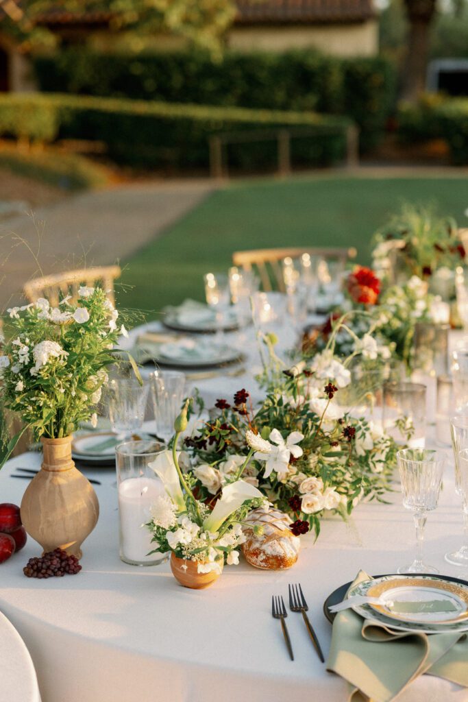 Elegant autumn dinner tablescape featuring green floral-patterned plates, gold flatware, and crystal glassware on a white linen tablecloth.